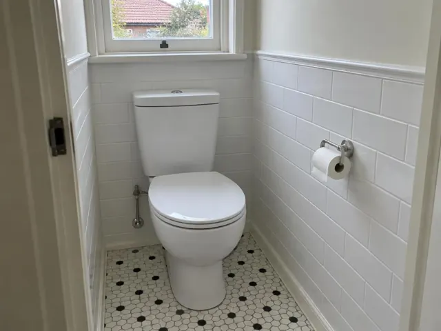 Clean working toilet in a small tiled bathroom with patterned floor and window in Vaucluse