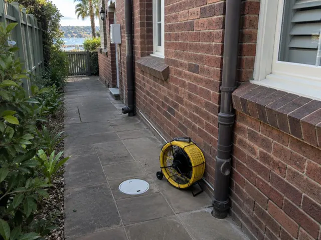 Brick side path with a capped drain inspection cover and a coiled yellow camera reel beside it in Vaucluse